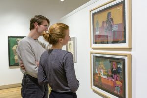 Two people looking at Eddie Arning paintings