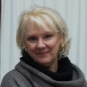 Photograph of a woman with short blonde hair, wearing a gray sweater
